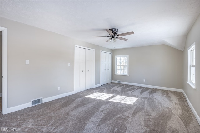 unfurnished bedroom with lofted ceiling, carpet floors, two closets, and ceiling fan