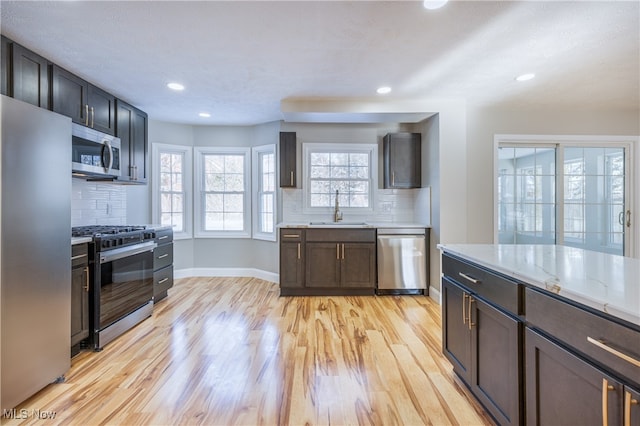 kitchen with light stone countertops, appliances with stainless steel finishes, decorative backsplash, sink, and light wood-type flooring