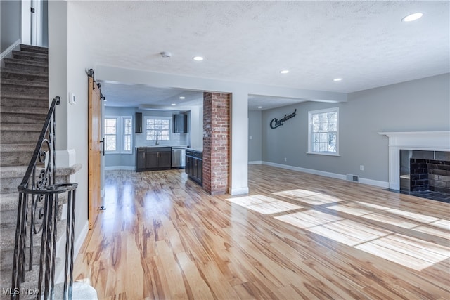 unfurnished living room featuring a barn door, light hardwood / wood-style flooring, a textured ceiling, and a healthy amount of sunlight