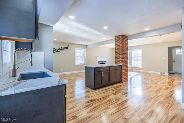 kitchen featuring a fireplace, sink, backsplash, light stone counters, and light hardwood / wood-style flooring