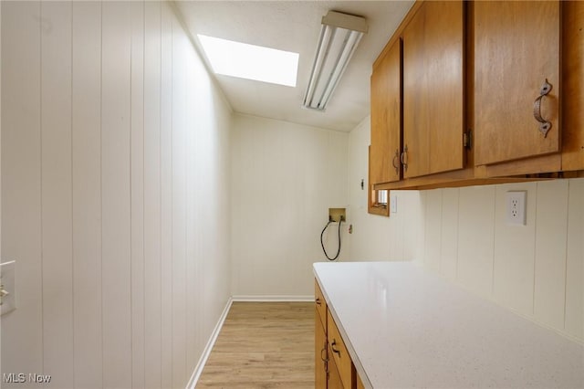 laundry area featuring wood walls, cabinets, a skylight, light hardwood / wood-style flooring, and washer hookup