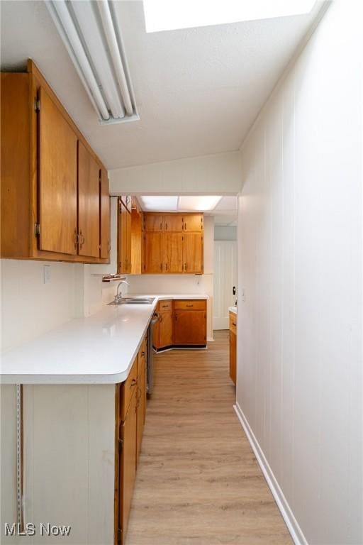 kitchen with vaulted ceiling with skylight, kitchen peninsula, sink, and light wood-type flooring