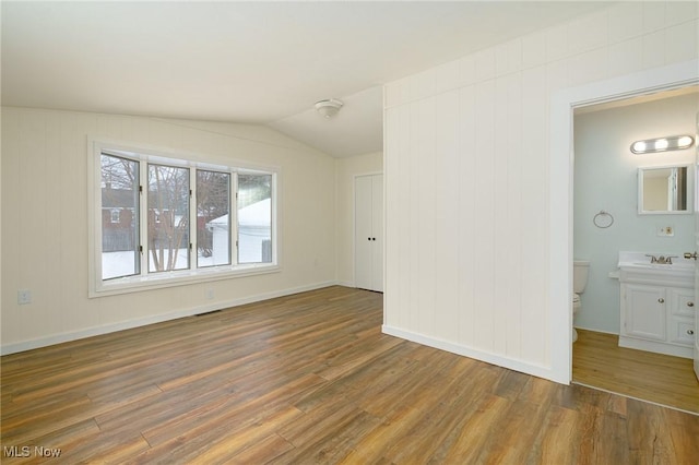 unfurnished bedroom featuring dark hardwood / wood-style floors, lofted ceiling, connected bathroom, and sink