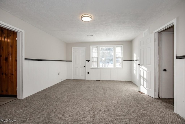 spare room featuring wood walls, carpet flooring, and a textured ceiling