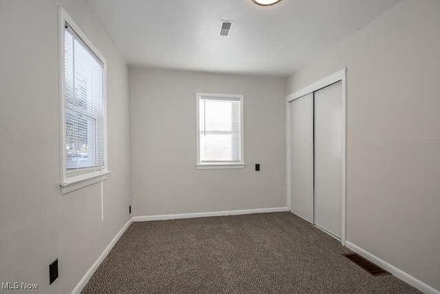 unfurnished bedroom featuring a closet, dark colored carpet, and multiple windows