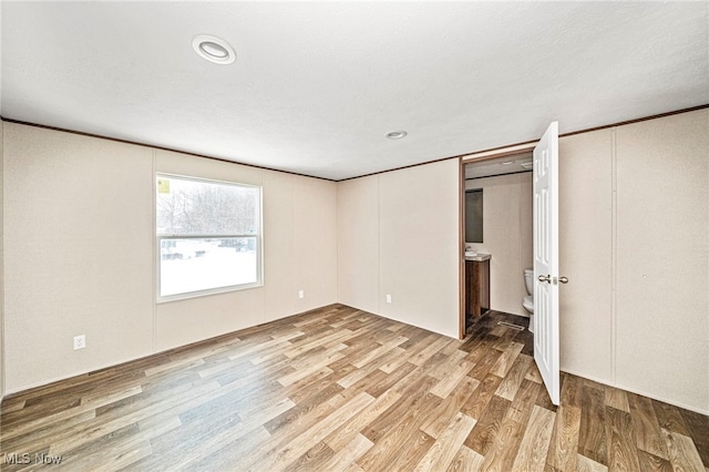 unfurnished bedroom with crown molding, connected bathroom, a textured ceiling, and light hardwood / wood-style floors