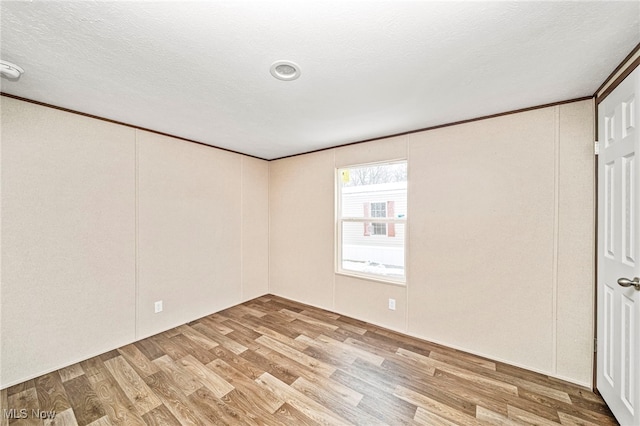 spare room featuring ornamental molding, light hardwood / wood-style floors, and a textured ceiling