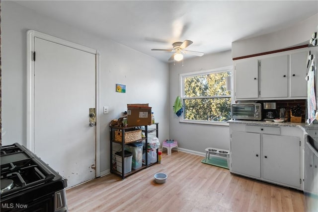 kitchen with ceiling fan, white cabinetry, light stone countertops, stove, and light hardwood / wood-style floors