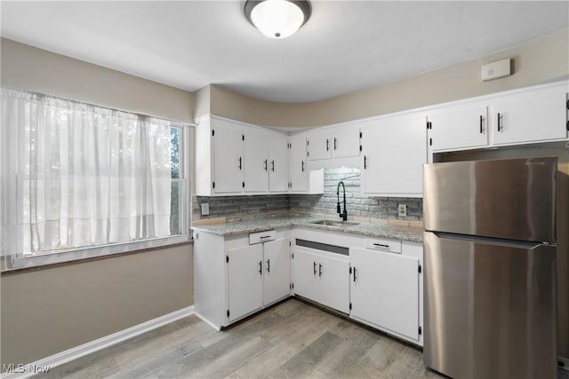 kitchen with light stone counters, sink, white cabinets, and stainless steel refrigerator