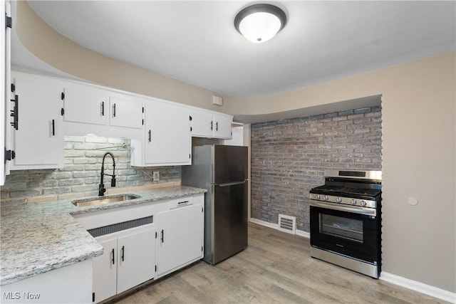 kitchen featuring sink, white cabinets, light wood-type flooring, brick wall, and stainless steel appliances