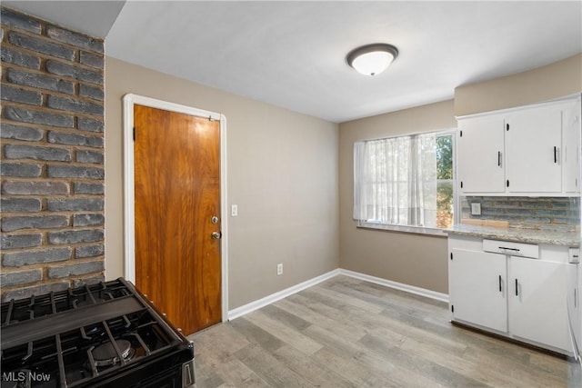 kitchen featuring black gas stove, tasteful backsplash, white cabinetry, light hardwood / wood-style flooring, and light stone counters