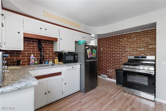 kitchen featuring fridge, white cabinetry, brick wall, stainless steel gas range, and sink