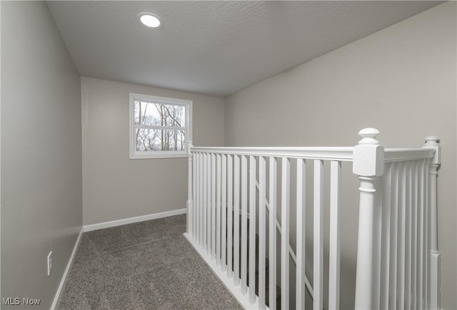 hall featuring dark colored carpet and a textured ceiling