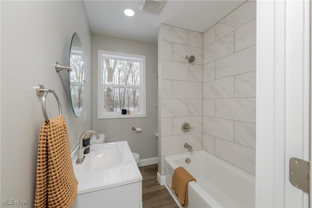 full bathroom with hardwood / wood-style floors, tiled shower / bath combo, vanity, and toilet