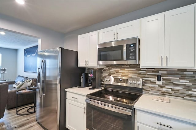 kitchen with white cabinets, backsplash, appliances with stainless steel finishes, and light hardwood / wood-style flooring