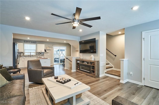 living room with ceiling fan, sink, and light wood-type flooring