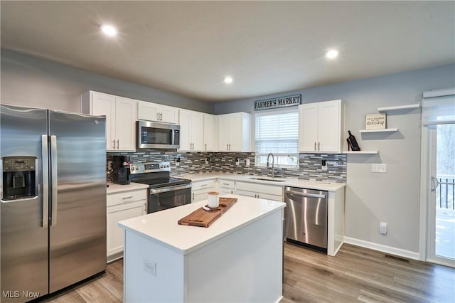 kitchen featuring white cabinets, stainless steel appliances, a kitchen island, and sink