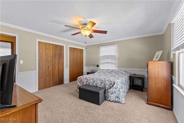 carpeted bedroom featuring ceiling fan, two closets, and crown molding