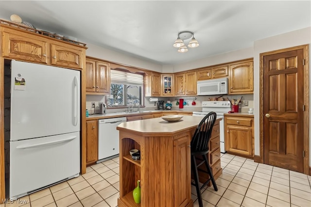 kitchen with sink, light tile patterned floors, white appliances, a kitchen bar, and a kitchen island