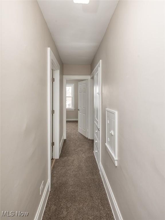 corridor with baseboards and dark carpet