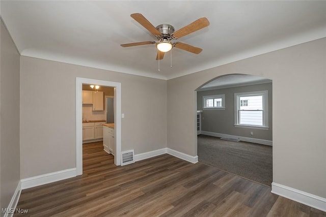 empty room featuring visible vents, dark wood finished floors, arched walkways, baseboards, and ceiling fan