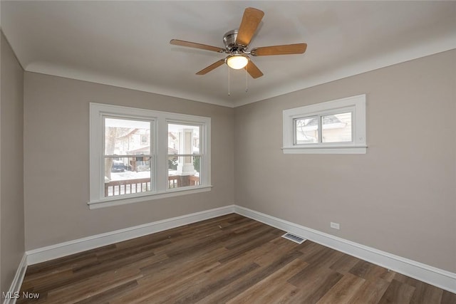 spare room with ceiling fan, visible vents, baseboards, and dark wood finished floors