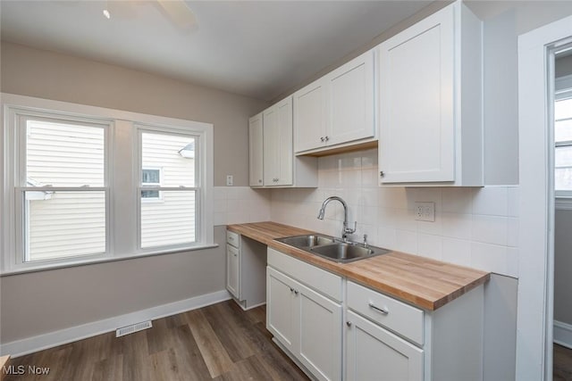 kitchen with visible vents, a sink, tasteful backsplash, baseboards, and wooden counters