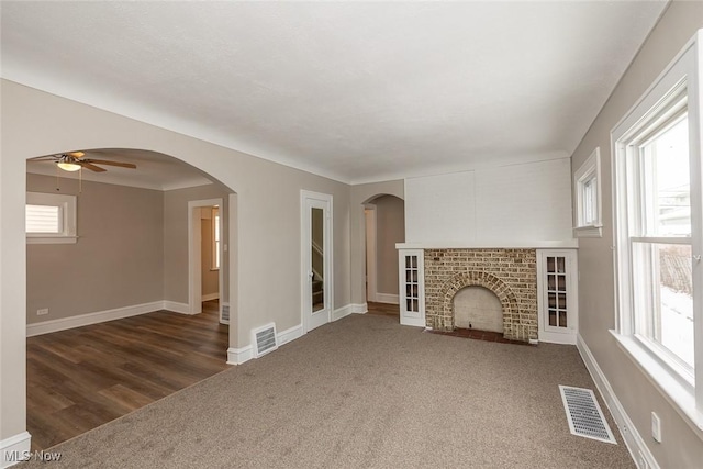 unfurnished living room with a fireplace, visible vents, and arched walkways