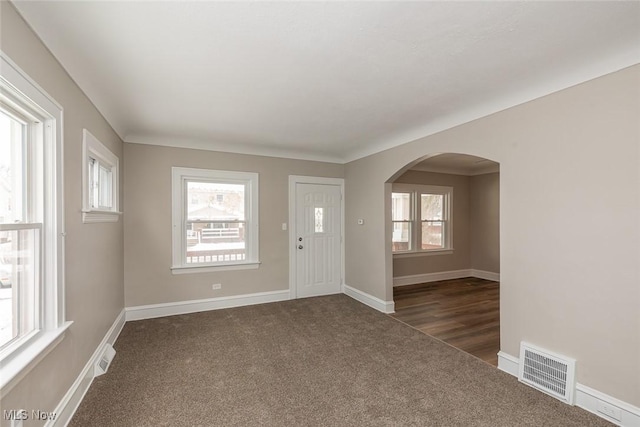 entrance foyer featuring arched walkways, visible vents, dark colored carpet, and baseboards