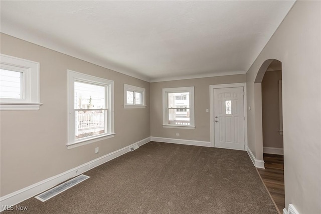 foyer entrance featuring arched walkways, visible vents, dark colored carpet, and baseboards