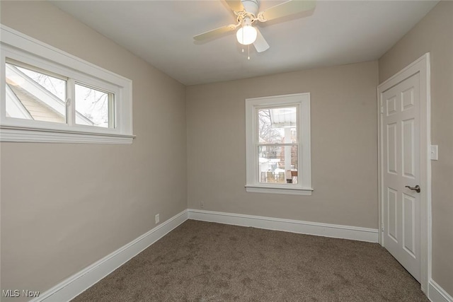 spare room with dark colored carpet, baseboards, and plenty of natural light