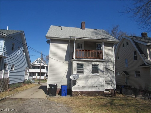 rear view of house with a shingled roof, a balcony, fence, and a chimney