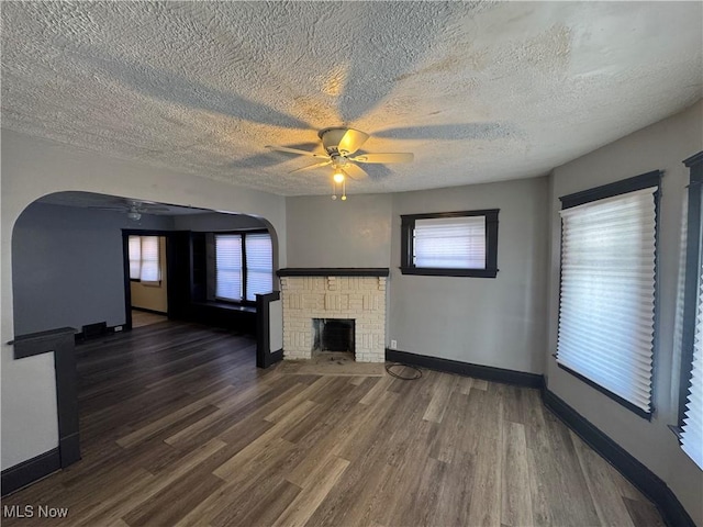 unfurnished living room with dark hardwood / wood-style floors, ceiling fan, a fireplace, and a textured ceiling