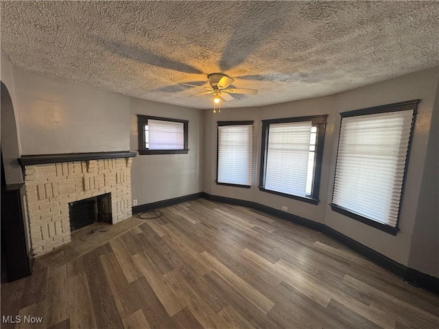 unfurnished living room featuring hardwood / wood-style flooring, ceiling fan, a brick fireplace, and a textured ceiling