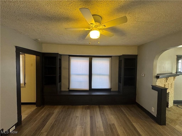 spare room featuring a fireplace, dark wood-type flooring, a textured ceiling, and ceiling fan