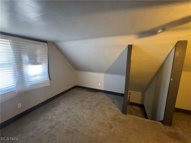 bonus room with lofted ceiling and dark carpet