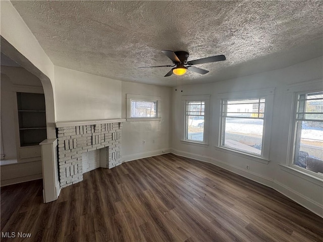 unfurnished living room with ceiling fan, dark hardwood / wood-style flooring, a brick fireplace, and a textured ceiling