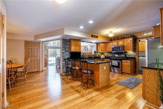 kitchen featuring washer / dryer, light wood-type flooring, appliances with stainless steel finishes, a kitchen breakfast bar, and decorative backsplash