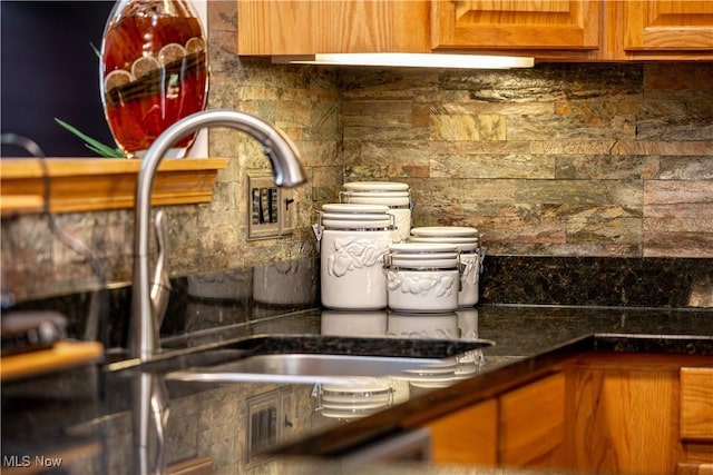 room details with sink, dark stone countertops, and backsplash