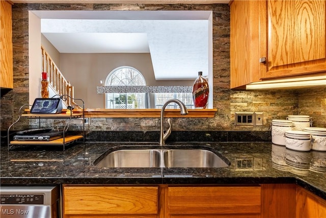 kitchen with dishwasher, dark stone countertops, brown cabinets, and a sink