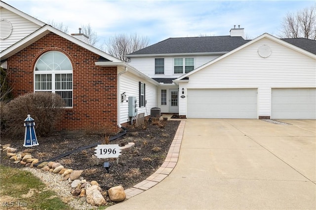 traditional home featuring a garage, driveway, brick siding, and a chimney