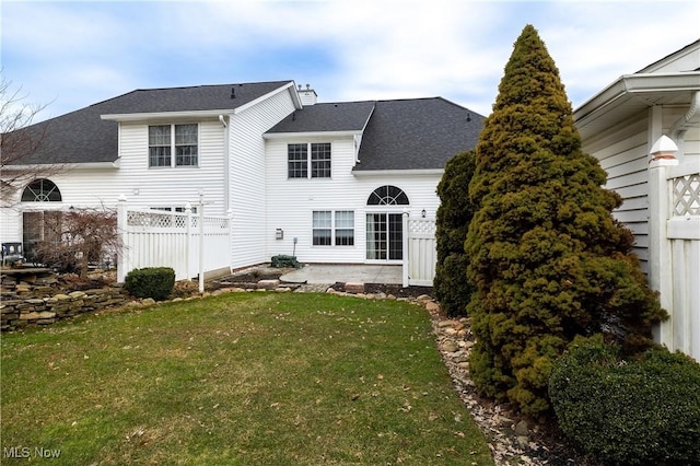 rear view of property featuring a shingled roof, a lawn, a chimney, and fence