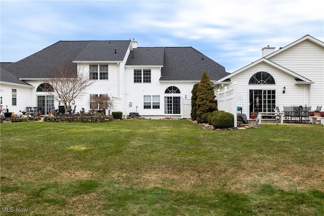 rear view of property with a yard, a chimney, a patio, and roof with shingles