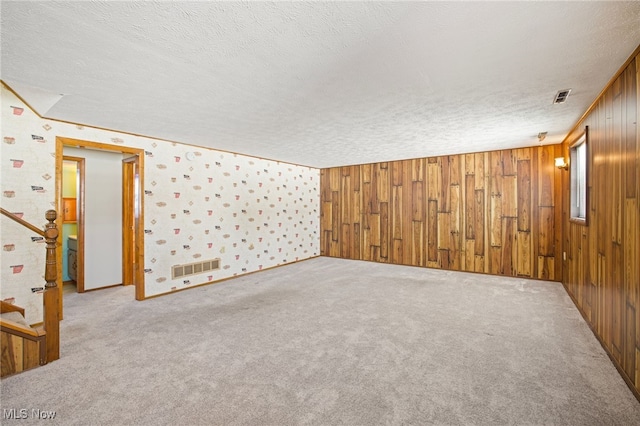 carpeted spare room with wood walls and a textured ceiling