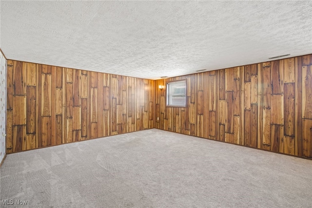 carpeted empty room featuring a textured ceiling and wood walls