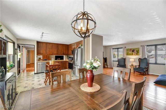 dining space with an inviting chandelier, light hardwood / wood-style floors, rail lighting, and a textured ceiling