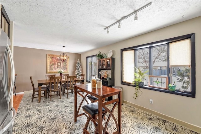 dining area with rail lighting, a notable chandelier, and a textured ceiling