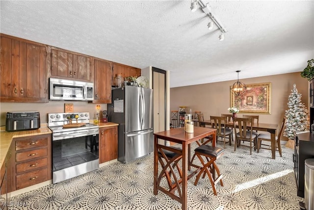 kitchen featuring rail lighting, hanging light fixtures, light tile patterned floors, stainless steel appliances, and a textured ceiling