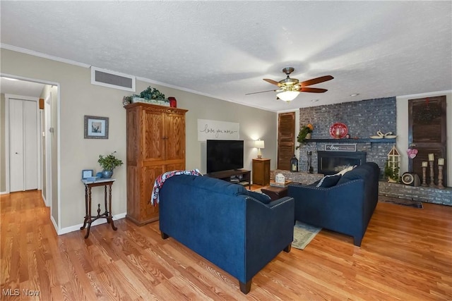 living room featuring crown molding, a brick fireplace, a textured ceiling, hardwood / wood-style flooring, and ceiling fan