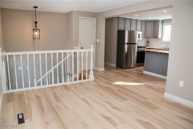 kitchen with wooden counters, backsplash, hanging light fixtures, light hardwood / wood-style floors, and stainless steel appliances